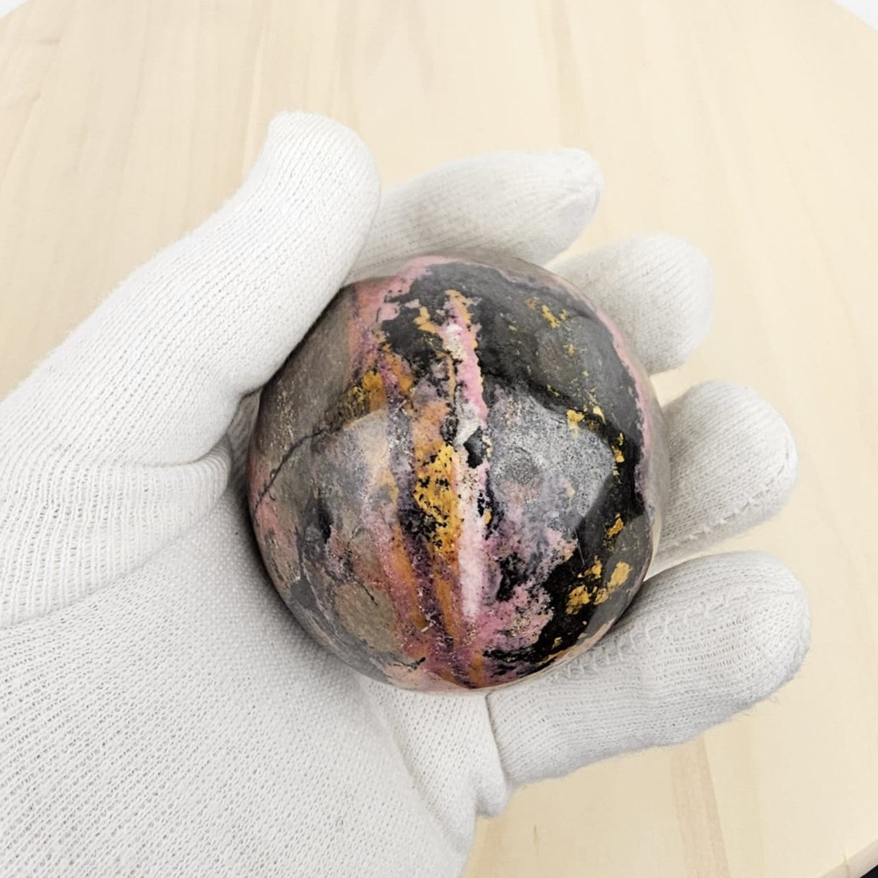 rhodonite crystal sphere holding in gloved hand with a beige background