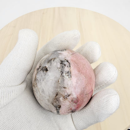 rhodonite crystal sphere held in a white glove on a light wooden surface