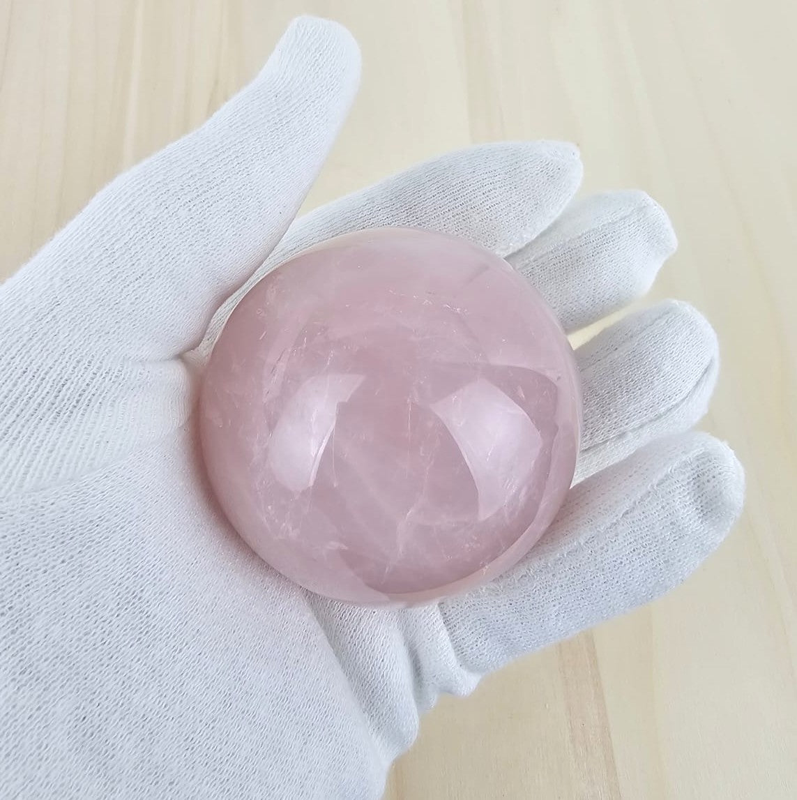 Rose quartz crystal sphere held in a white glove on a light wooden background