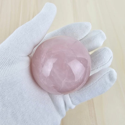 Rose quartz crystal sphere held in a white glove on a light wooden background