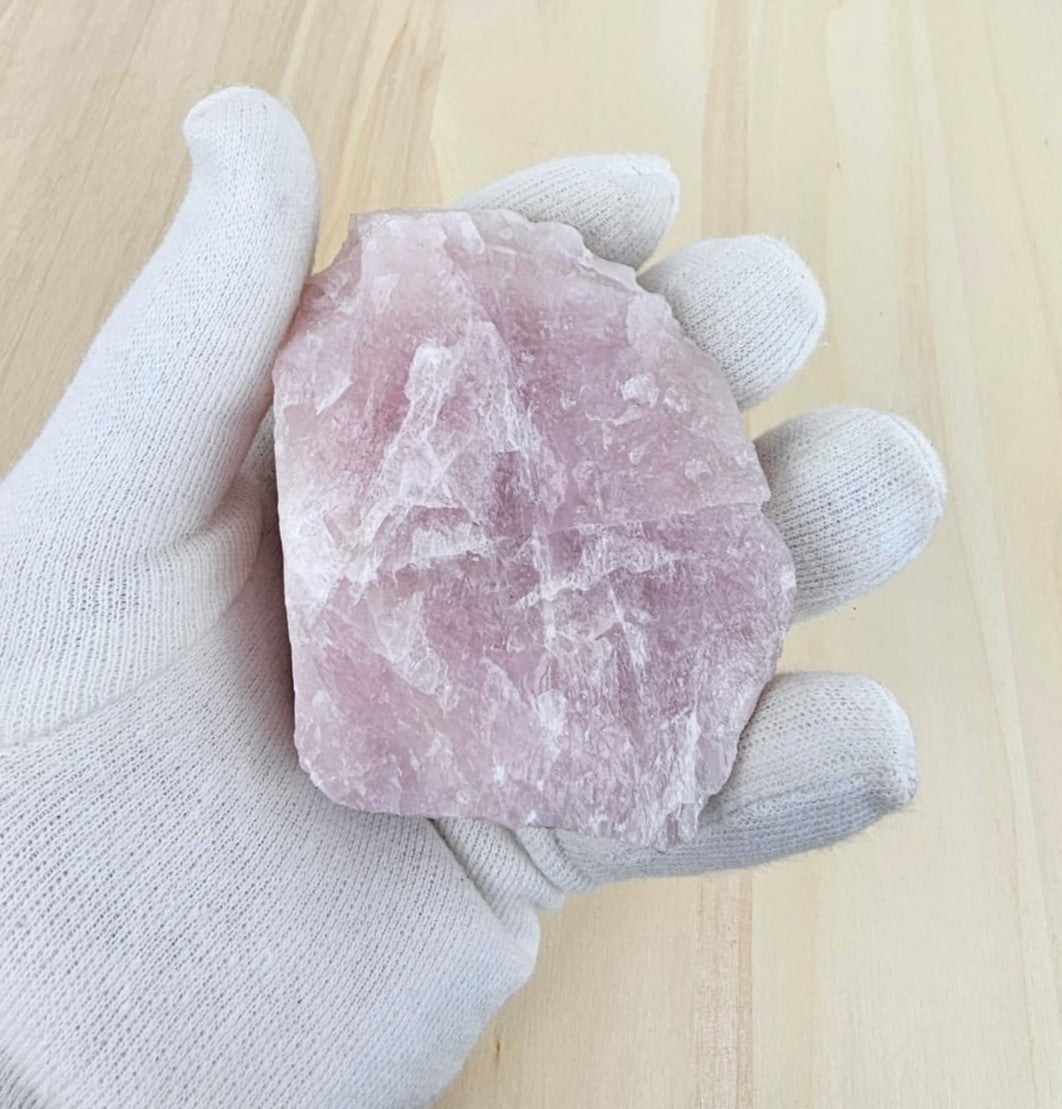 Hand wearing a white glove holding a rose quartz on a light wooden surface