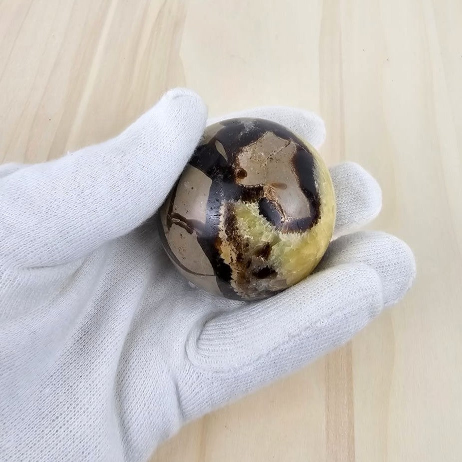 Hand holding a septarian sphere against a light wooden background