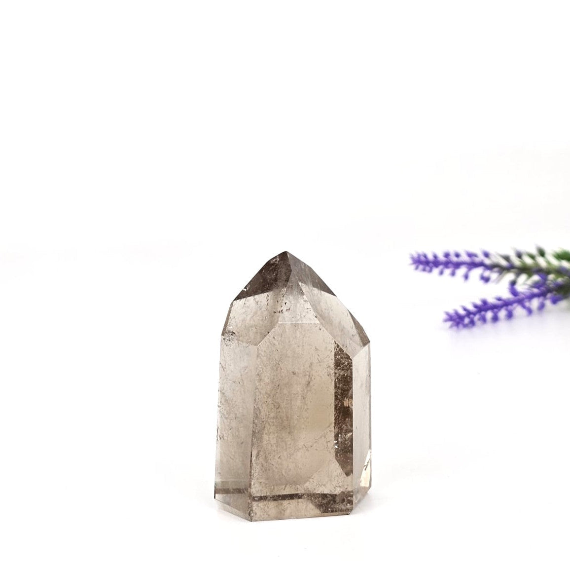 Smoky quartz crystal tower on a white background with a sprig of lavender.