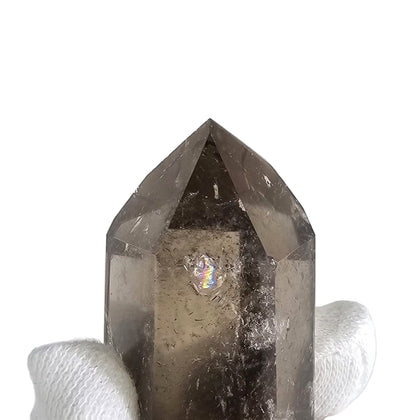 Smoky crystal pyramid held by a gloved hand on a white background