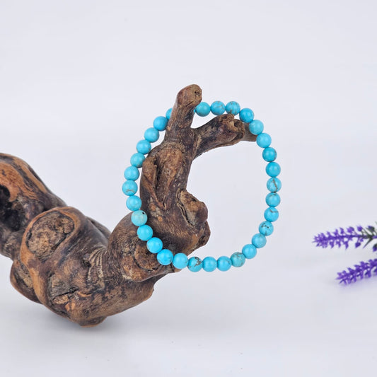 Turquoise beaded bracelet on a piece of driftwood with a white background